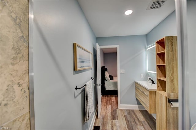 ensuite bathroom featuring wood finished floors, vanity, and baseboards