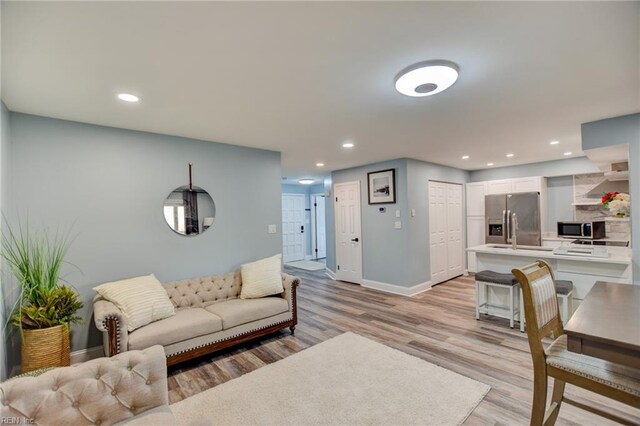 living area featuring baseboards, light wood finished floors, and recessed lighting