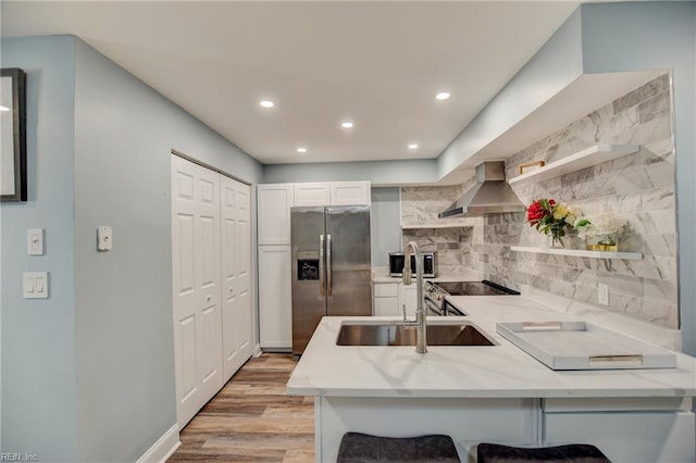 kitchen featuring stainless steel appliances, wall chimney range hood, a sink, light stone countertops, and a peninsula