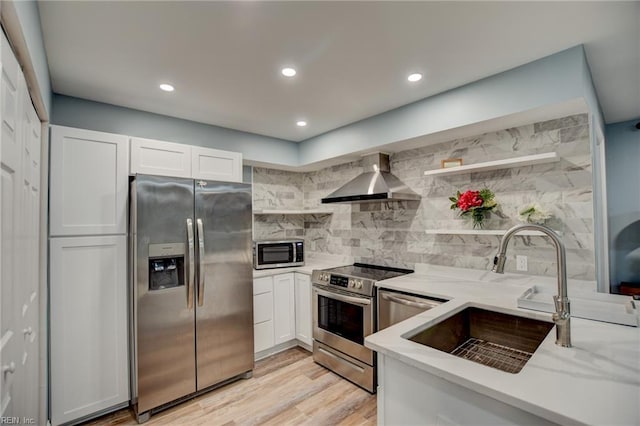 kitchen featuring stainless steel appliances, open shelves, wall chimney exhaust hood, a sink, and white cabinetry