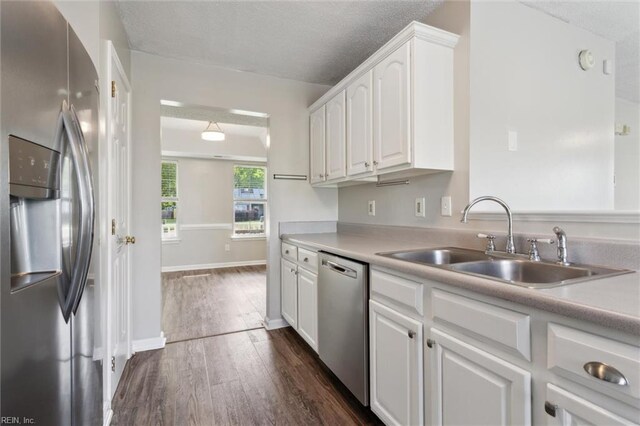 kitchen with stainless steel appliances, a sink, white cabinets, dark wood-style flooring, and light countertops
