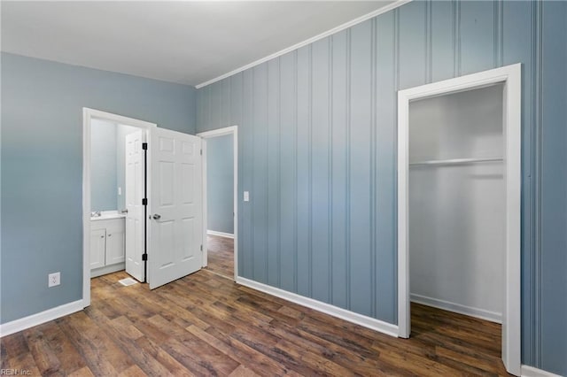 unfurnished bedroom featuring a closet, dark wood finished floors, baseboards, ornamental molding, and connected bathroom