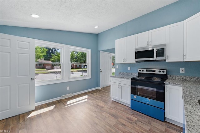 kitchen with stainless steel microwave, black range with electric stovetop, a textured ceiling, light wood-style flooring, and white cabinets