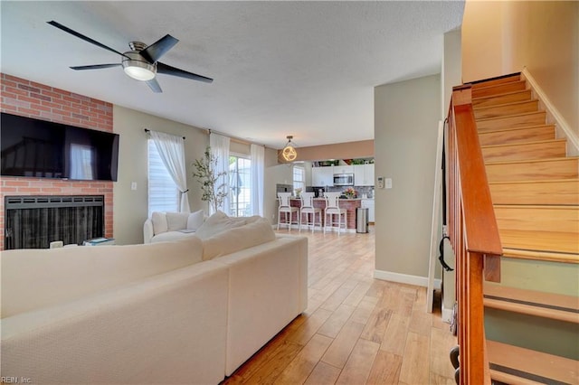 100 Castilian Dr, Virginia Beach, VA 23462 - living room with ceiling fan, stairs, light wood-style floors, a brick fireplace, and baseboards