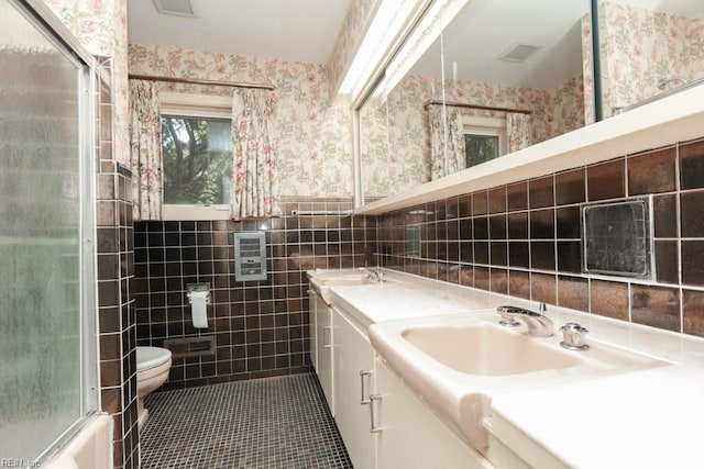 6025 River Rd, Norfolk, VA 23505 - full bathroom featuring wallpapered walls, tile walls, toilet, double vanity, and a wainscoted wall