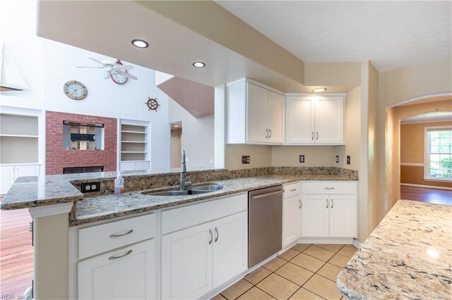 kitchen with stainless steel dishwasher, a sink, arched walkways, white cabinets, and light stone countertops