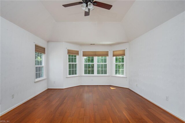 unfurnished room with a ceiling fan, vaulted ceiling, wood finished floors, healthy amount of natural light, and baseboards