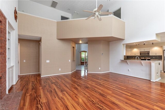 unfurnished living room featuring a ceiling fan, wood finished floors, a towering ceiling, arched walkways, and baseboards
