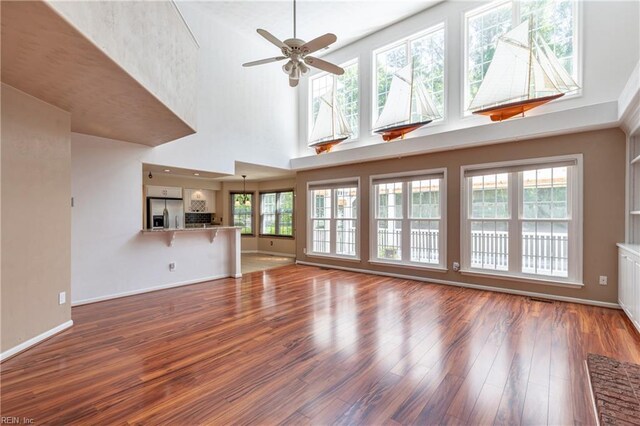 unfurnished living room with wood finished floors, a ceiling fan, baseboards, and a towering ceiling
