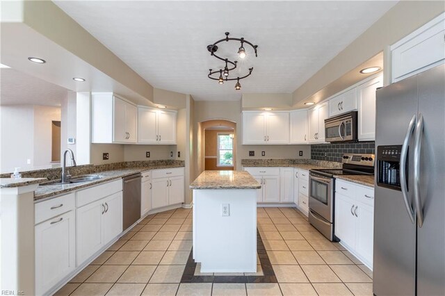 kitchen featuring stainless steel appliances, a sink, arched walkways, a center island, and white cabinetry