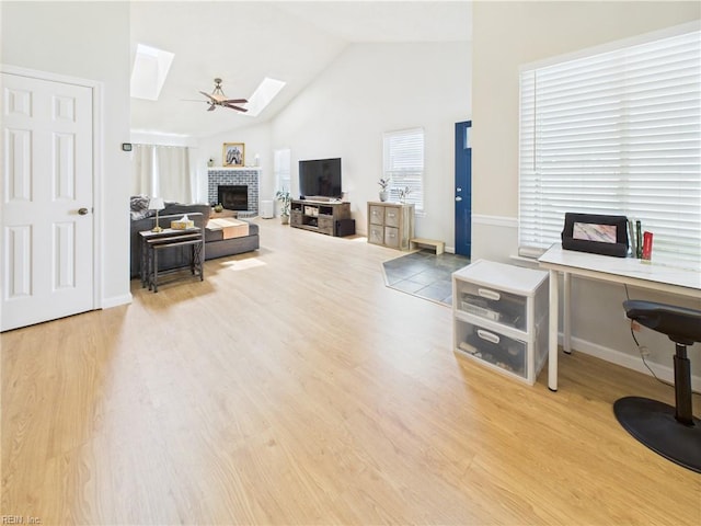 living room with a skylight, a brick fireplace, high vaulted ceiling, wood finished floors, and a desk