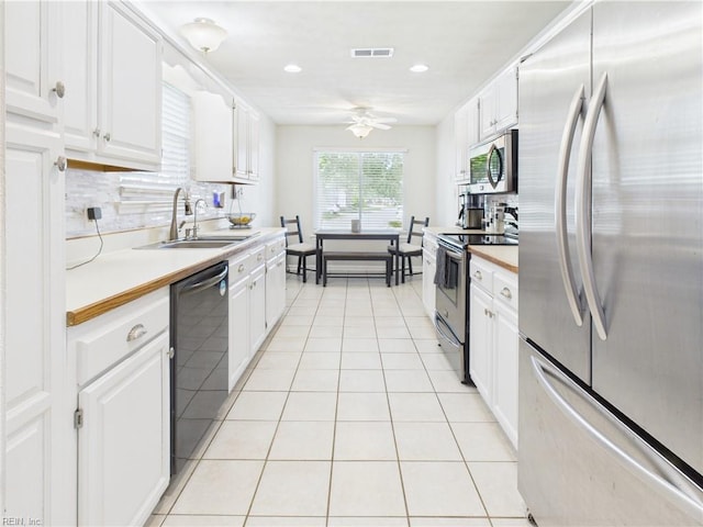 kitchen featuring appliances with stainless steel finishes, a sink, a ceiling fan, white cabinets, and light tile patterned floors