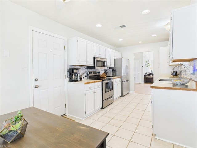kitchen with appliances with stainless steel finishes, a sink, light tile patterned floors, white cabinetry, and recessed lighting
