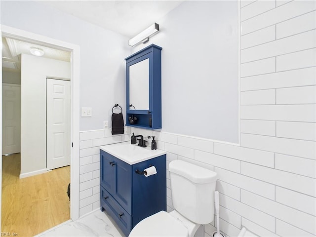 half bath featuring tile walls, toilet, vanity, and wainscoting