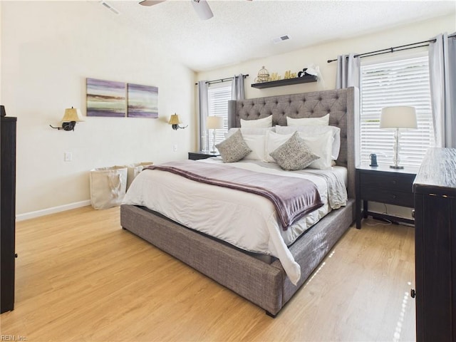 bedroom with light wood-style flooring, multiple windows, a textured ceiling, baseboards, and a ceiling fan