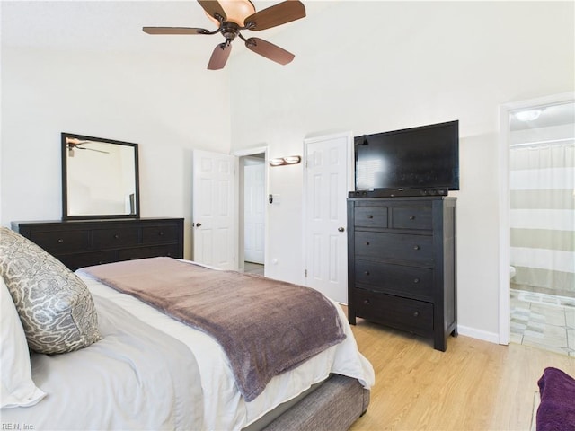 bedroom featuring light wood-style floors, ensuite bathroom, a towering ceiling, baseboards, and ceiling fan