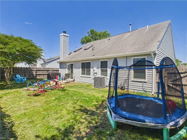back of house with a trampoline, central AC unit, and a shingled roof