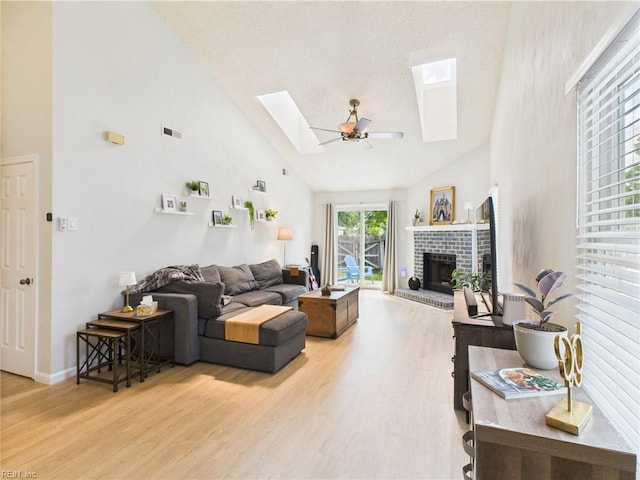 living area featuring a skylight, high vaulted ceiling, light wood-type flooring, a brick fireplace, and baseboards