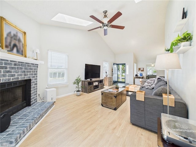 living room with a skylight, a fireplace, high vaulted ceiling, light wood finished floors, and ceiling fan