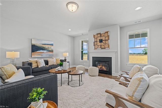 living room featuring wood finished floors, a glass covered fireplace, baseboards, and recessed lighting