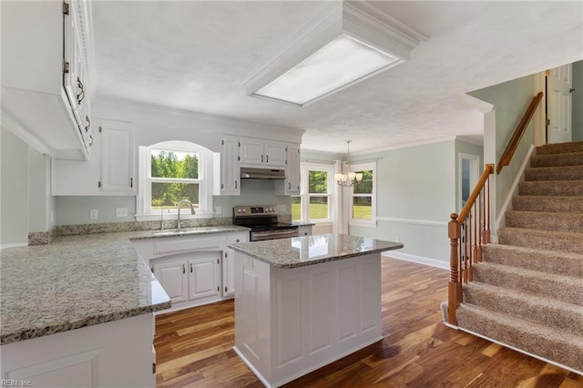 kitchen featuring stainless steel electric range oven, under cabinet range hood, a center island, white cabinets, and ornamental molding