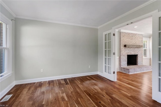unfurnished living room with wood finished floors, baseboards, a brick fireplace, crown molding, and french doors