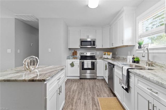 kitchen featuring appliances with stainless steel finishes, white cabinets, light wood finished floors, light stone counters, and a sink