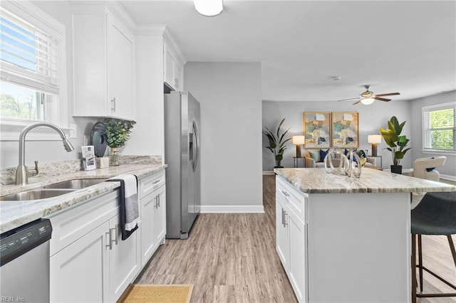 kitchen with appliances with stainless steel finishes, a sink, a breakfast bar, ceiling fan, and light wood-style floors