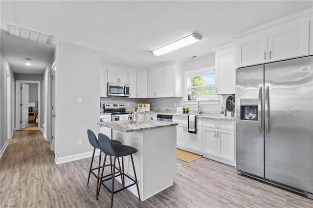 kitchen featuring stainless steel appliances, light wood finished floors, a kitchen bar, and white cabinetry