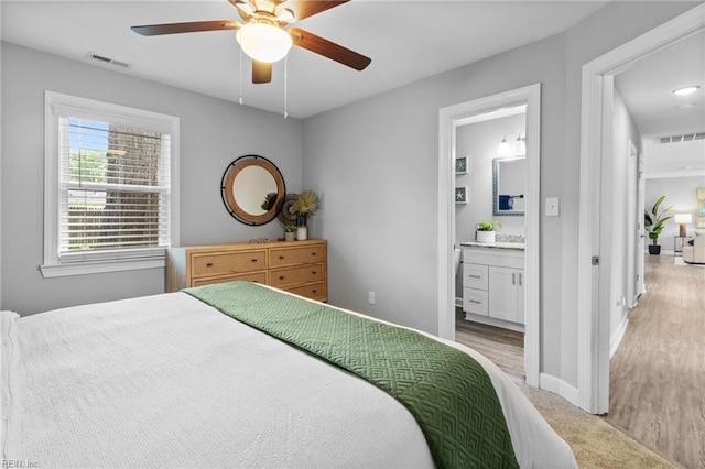 bedroom featuring baseboards, connected bathroom, a ceiling fan, and light wood-style flooring