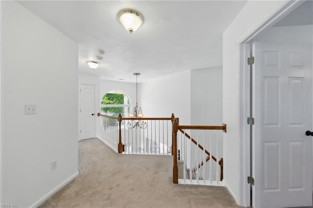 corridor with carpet floors, an upstairs landing, baseboards, and a chandelier