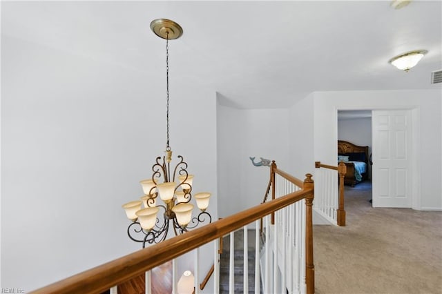 hall featuring a chandelier, an upstairs landing, carpet floors, and baseboards