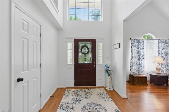 entryway featuring light wood-style floors, plenty of natural light, a towering ceiling, and baseboards