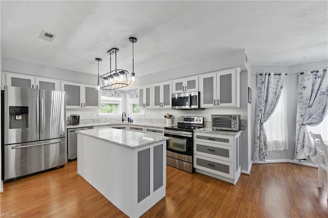 kitchen with appliances with stainless steel finishes, a center island, white cabinets, light stone counters, and pendant lighting