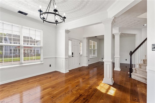 unfurnished dining area with wood-type flooring, a chandelier, crown molding, decorative columns, and stairs