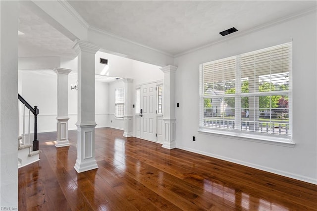 unfurnished living room featuring dark wood-type flooring, baseboards, ornamental molding, ornate columns, and stairs