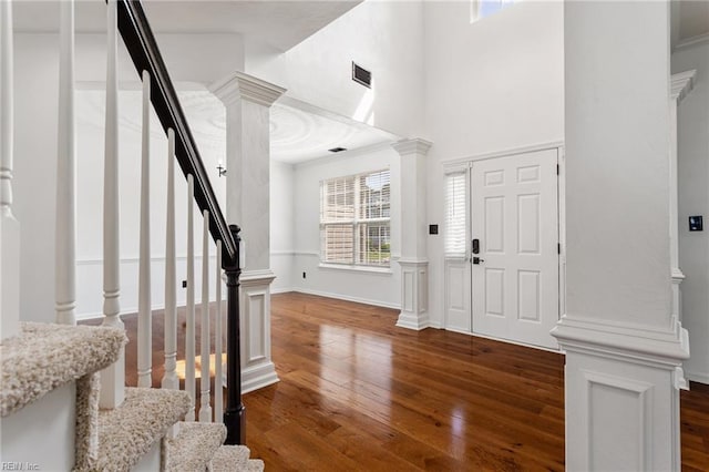 foyer featuring dark wood-style flooring, stairway, decorative columns, a high ceiling, and crown molding