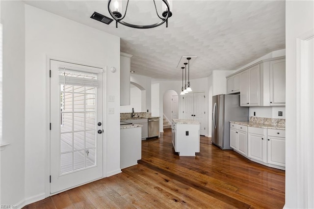 kitchen featuring arched walkways, stainless steel appliances, a kitchen island, a sink, and dark wood-style floors