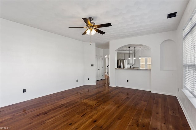 unfurnished living room with ceiling fan, dark wood-style floors, arched walkways, a sink, and baseboards