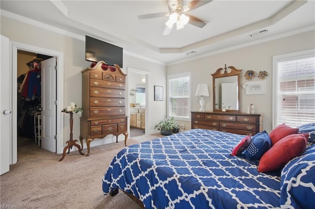 carpeted bedroom with a tray ceiling, a spacious closet, crown molding, connected bathroom, and ceiling fan