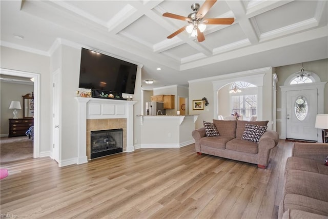 living room with coffered ceiling, light wood-type flooring, ceiling fan, a tiled fireplace, and beam ceiling