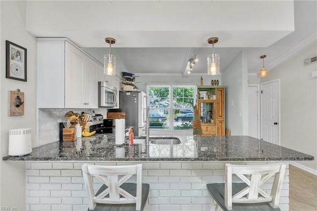kitchen featuring stainless steel appliances, a peninsula, dark stone countertops, a sink, and white cabinets