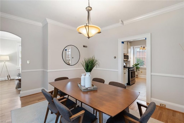 dining area with arched walkways, light wood-type flooring, crown molding, and baseboards