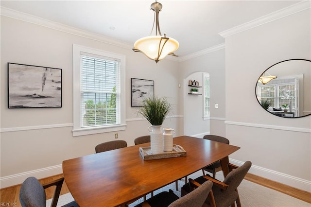 dining space featuring wood finished floors, ornamental molding, baseboards, and arched walkways