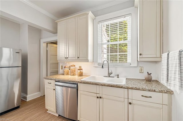 kitchen featuring appliances with stainless steel finishes, a sink, light wood finished floors, baseboards, and crown molding