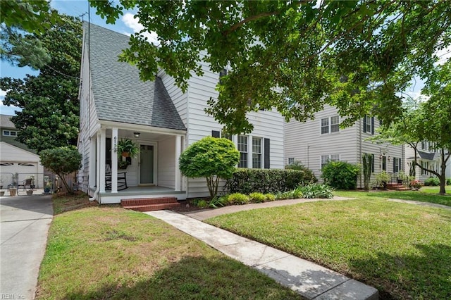 view of front of home with covered porch, a shingled roof, an outbuilding, and a front yard