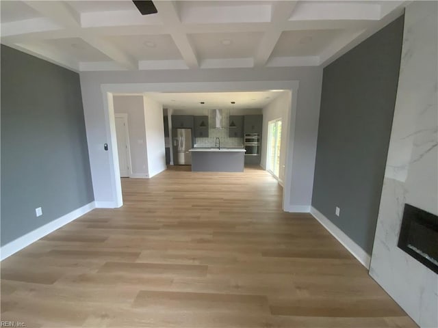 unfurnished living room with coffered ceiling, baseboards, beam ceiling, light wood-type flooring, and a sink