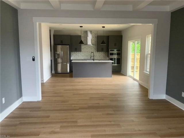 kitchen with stainless steel appliances, decorative backsplash, wall chimney range hood, light countertops, and baseboards