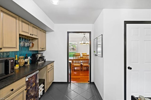 kitchen featuring stainless steel microwave, dark tile patterned flooring, dark countertops, cream cabinetry, and a chandelier