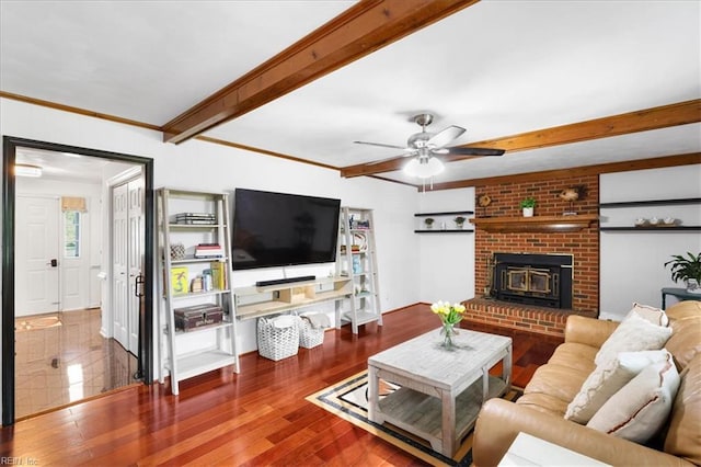 living area featuring beam ceiling, a ceiling fan, wood finished floors, a brick fireplace, and crown molding